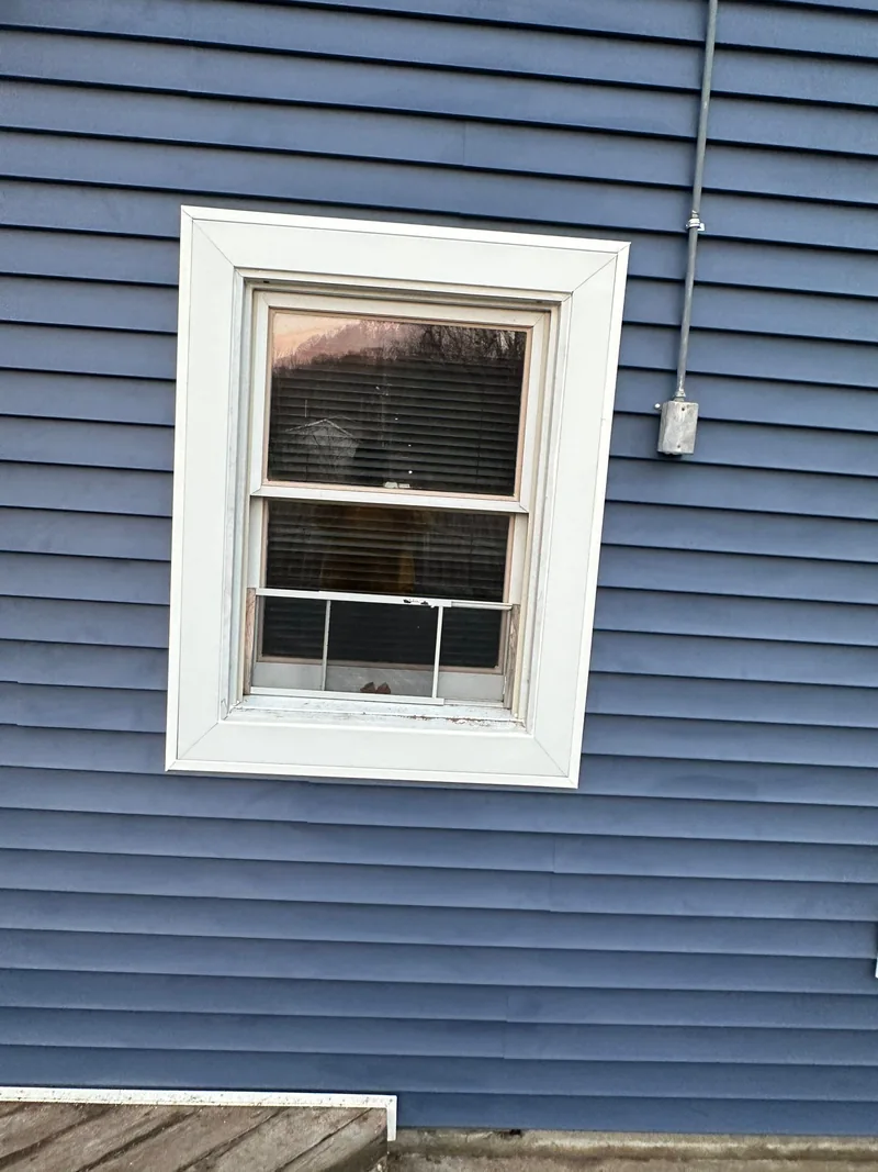 Blue horizontal siding and white trim around an existing window on a CPG siding project